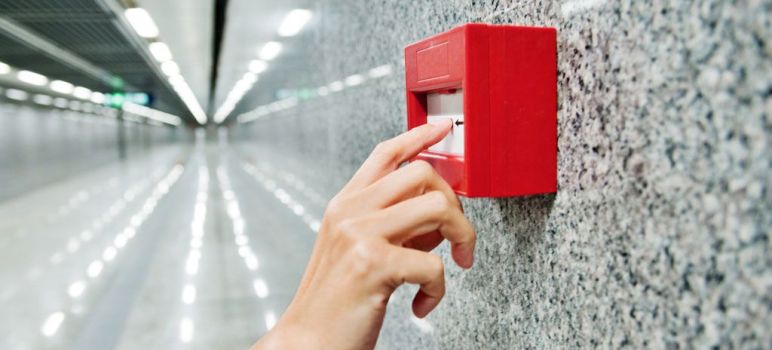 Hand löst einen roten Feuermelder an einer Wand aus, wie in einer Brandschutzhelfer Ausbildung geübt